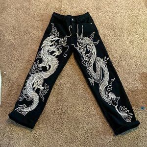 black jeans with white dragon print along the front side of the jeans.